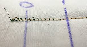A piece of fabric that has been stitched on a sewing machine. The bottom thread is looped above the fabric, while the top thread lies flat on top.
